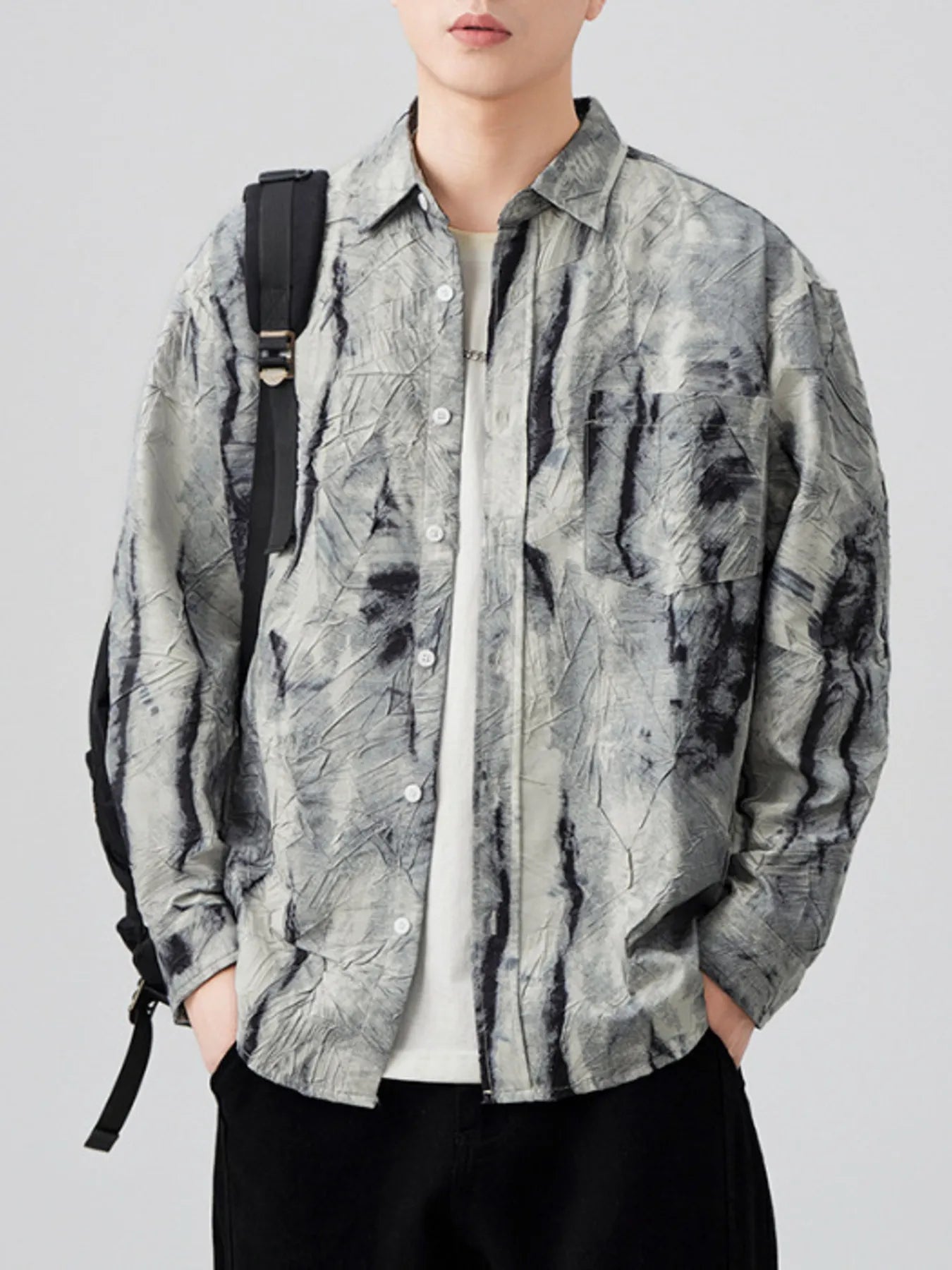 Person wearing a brown and white tie-dye shirt with a backpack on a plain background