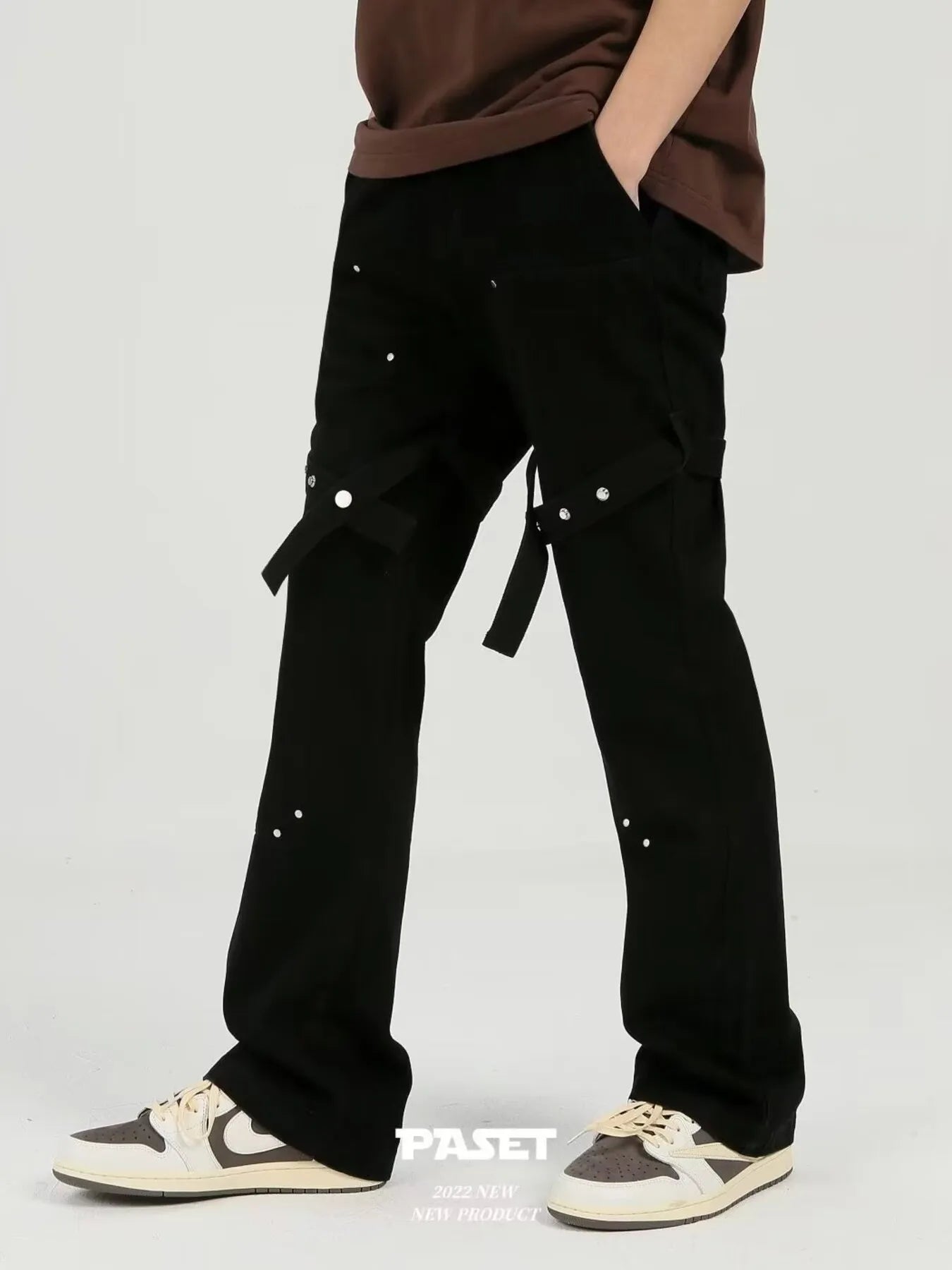 Person wearing black studded cargo pants with a belt on a plain background.