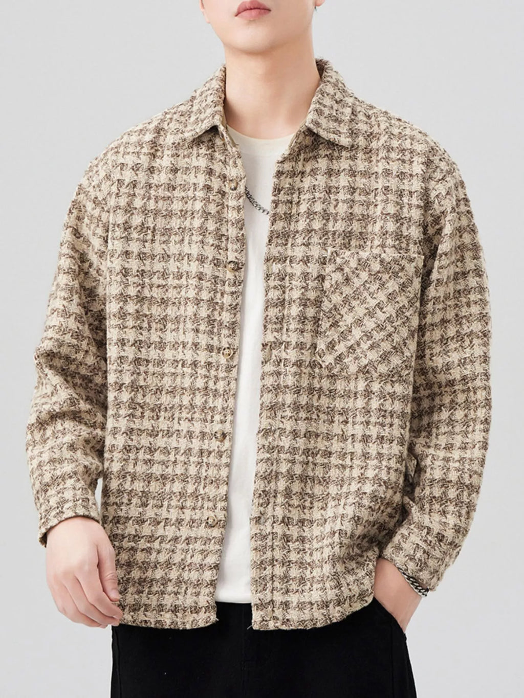 Person wearing a patterned shirt over a plain shirt on a light gray background