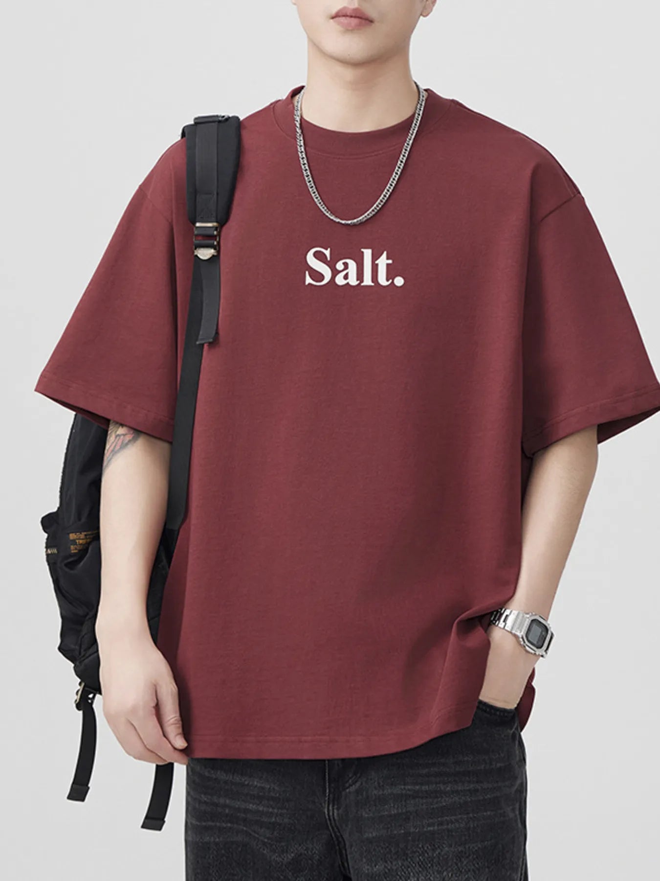 Person wearing a maroon t-shirt with 'Salt.' text, carrying a black backpack on a light gray background