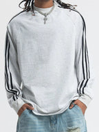 Person wearing a white shirt with black stripes on sleeves and light blue jeans.